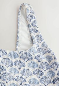 Sac en tissu blanc texturé avec une large bandoulière, décoré de motifs répétitifs de coquillages bleus de différentes nuances.