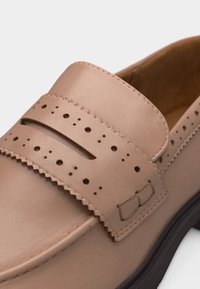 Ταμπά δερμάτινο μοκασίνι με διάτρητες λεπτομέρειες και διακοσμητική ραμμένη αγκράφα στο λουράκι, με μαύρη σόλα.