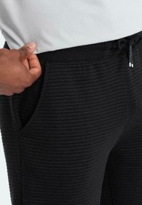 Pantaloni jogger neri a coste con tasche laterali e vita con lacci, caratterizzati da un tessuto testurizzato e una vita piatta.