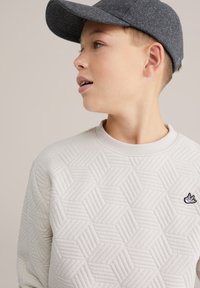 Világosszürke pulóver hatszögletű mintával és bordázott kerek nyakkivágással. Fekete hímzett logó a bal mellrészen. Szürke szövet sapka.