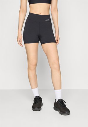 Schwarze Sportshorts mit hohem Bund, glatter Textur und kleinem "STRONGER"-Logo. Kombiniert mit schwarzen Turnschuhen und weißen Socken.