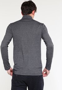 Graues Langarmshirt mit hohem Kragen, aus texturiertem Stoff. Hat ein tailliertes Design und eine glatte Verarbeitung am Saum.