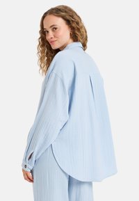 Lichtblauwe, oversized, lange mouwen shirt gemaakt van gestructureerde stof. Voorzien van een met knopen sluitende manchette en een ronde zoom.