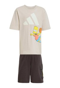 Camiseta de algodón beige con un gran logo blanco de Adidas y un dibujo de Bart Simpson con un balón de baloncesto. Combinada con pantalones cortos oscuros con bolsillos.