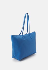 Sac fourre-tout bleu avec une texture lisse, forme rectangulaire, deux longues poignées et une ouverture zippée. Présente des détails de couture subtils.