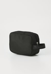 Svart nylon toalettmappe med rektangulær form, glidelås og en merket stoffhåndtak med "TOMMY" i kontrastfarge.