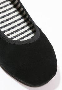 Chaussure plate noire avec bout arrondi et bordure élastique noire, dotée d'une doublure intérieure en tissu rayé noir et blanc.