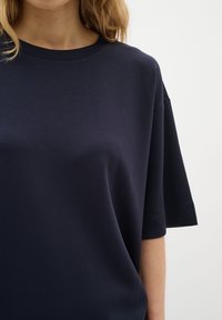 Sötétkék, rövid ujjú póló puha anyagból, laza fazonnal és kerek nyakkal, sima textúrával és egyszerű dizájnnal.