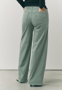Široké nohavice svetlozelené farby z mäkkej látky, s vreckami na zadnej strane a hladkou textúrou, s priliehavým strihom okolo pásu.