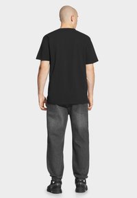 Czarna bawełniana koszulka z krótkim rękawem, w połączeniu z ciemnoszarymi dżinsami. Stylizacja dopełniają czarne buty sportowe.