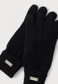 Czarne dziergane rękawiczki z prążkowanymi mankietami, o gładkiej fakturze i metalowej etykiecie z napisem "don't waste culture."