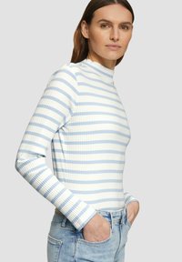Gestreifter Langarm-Top in Hellblau und Weiß. Mit hohem Kragen und figurbetonter Silhouette. Kombiniert mit hellen Jeans.