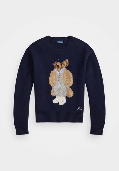 Marineblauwe trui met een gedetailleerde geborduurde beer die een beige jas en grijze broek draagt, afgewerkt met geribde manchetten en een ronde hals.