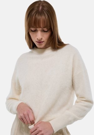 Pull crème avec une texture douce et duveteuse, col montant et épaules tombantes. Manches longues avec des poignets ajustés.