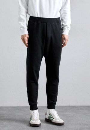 Black sweatpants made of a soft material, featuring a tapered design, elastic waistband, and side seams. Worn with white and green sneakers.