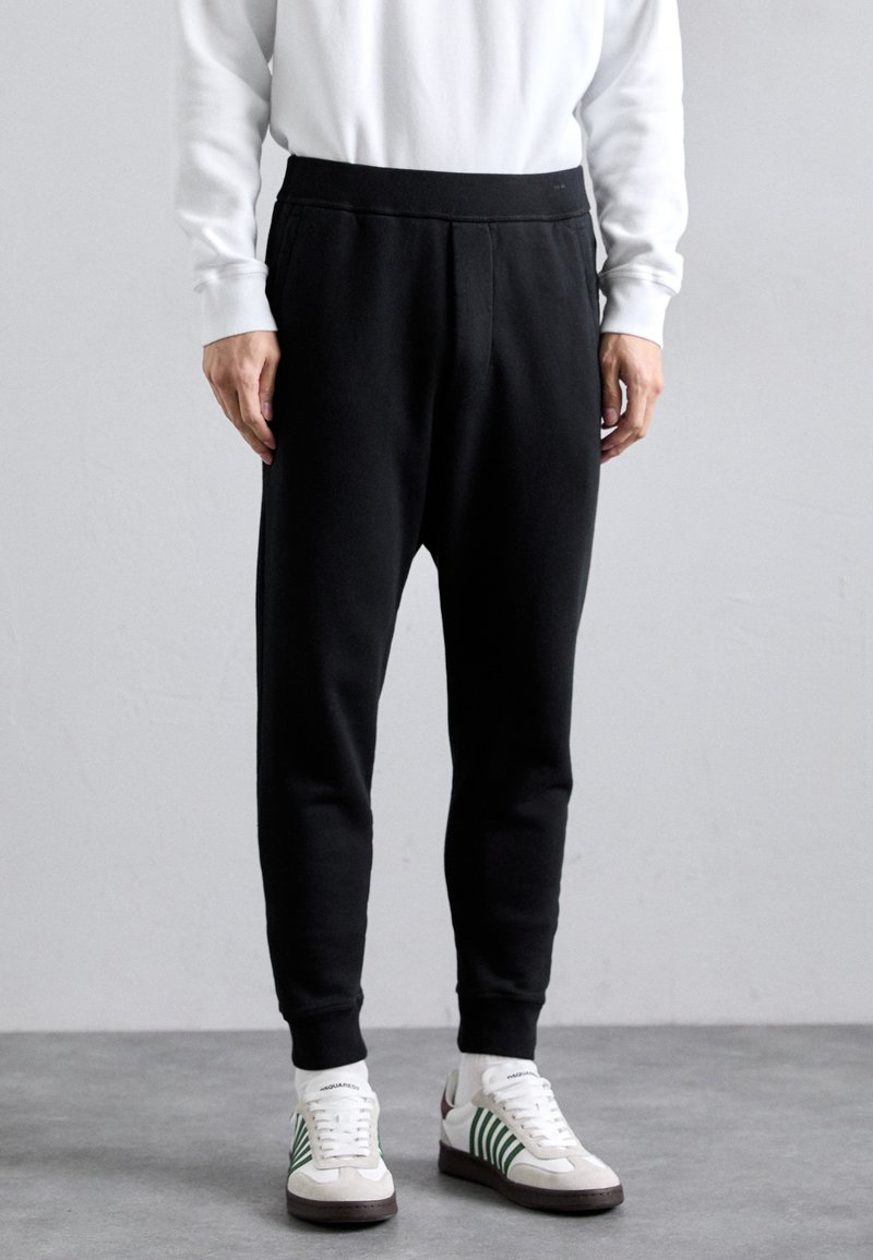 Black sweatpants made of a soft material, featuring a tapered design, elastic waistband, and side seams. Worn with white and green sneakers.