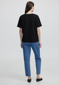 T-shirt nera in cotone con scollatura a girocollo, vestibilità ampia, abbinata a jeans in denim blu, con gamba dritta e orli leggermente sfilacciati.