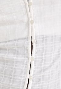 Close-up of a white textured shirt with small buttons, showing a gap between two button fastenings.