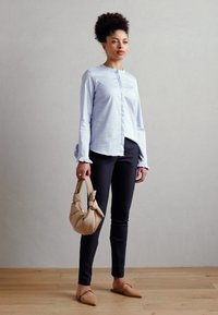 Camicia azzurro chiaro con maniche a volant, pantaloni neri aderenti e una borsa beige annodata. Ballerine color cuoio completano il look.