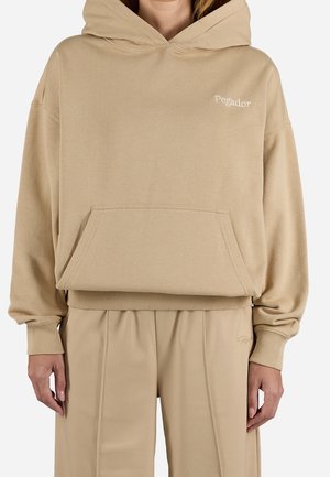 Beige hooded sweatshirt with front pocket and "Pegador" logo worn with matching beige pants, shown from neck to mid-thigh.