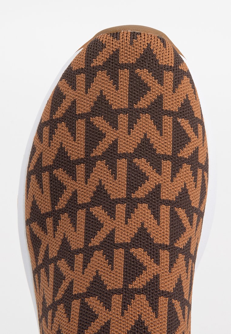 Texturierter brauner Strickschlüpfschuh mit dunklem geometrischen Muster und weißer Sohle. Verfügt über eine runde Zehenform und eine elastische Passform.