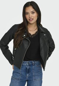 Veste de moto en cuir noir avec quincaillerie en argent, poches zippées et design ajusté, associée à un haut noir avec des dentelles et un jean taille haute.