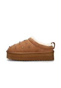 Pantofole in camoscio marrone con fodera in pelliccia sintetica color crema, suola spessa e borchie decorative color oro rosa sulla superficie superiore. Presenta una linguetta posteriore.