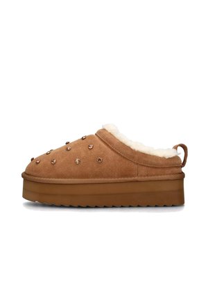 Pantofole in camoscio marrone con fodera in pelliccia sintetica color crema, suola spessa e borchie decorative color oro rosa sulla superficie superiore. Presenta una linguetta posteriore.
