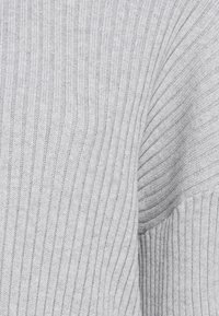 Lichtgrijze ribgebreide stof met een gestructureerd patroon, voorzien van verticale en diagonale lijnen die een gevouwen of gedrapeerd effect creëren.