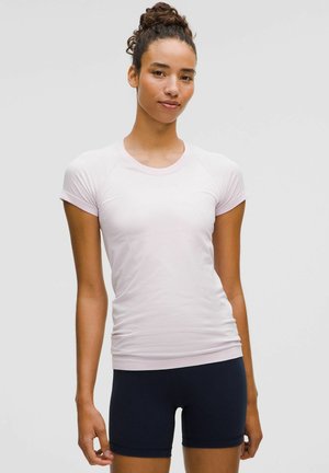Maglietta atletica corta rosa chiaro con maniche corte, colletto rotondo e design aderente, abbinata a pantaloni corti blu scuro. Tessuto morbido con leggera texture.
