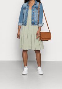 Ljusgrön lager-på-lager klänning, denimjacka med kopparfärgade knappar, brun crossbody-väska och vita sneakers. Totalt avslappnad och lager-på-lager stil.