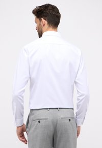 Witte lange mouwen shirt met een standaard kraag, gladde textuur. Gecombineerd met lichtgrijze broek met twee achterzakken en knoopaccenten.