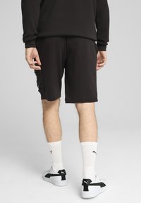 Black shorts made of soft fabric, featuring a side pocket. The model wears white socks and sporty black and white shoes.