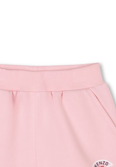 Pantalons de sudation en coton rose avec taille côtelée, poches latérales et un patch logo circulaire sur la jambe inférieure gauche.