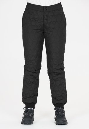 Zwarte doorgestikte broek met elastische tailleband, knoopsluiting, omgeslagen enkels, gedragen met zwarte wandelschoenen en witte sokken.