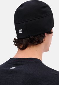 Zwarte gebreide beanie met een gladde textuur en een laag profiel, met een klein wit logo aan de achterkant.