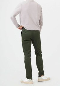 Gröna byxor med smal passform, med bakfickor och ett mjukt tyg. Matching med en ljusgrå tröja och vita sneakers.