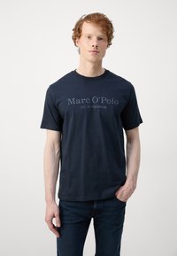 Tumsā zila īsām piedurknēm T-krekls no kokvilnas, ar grafisku uzdruku, kas krūtīs saka "Marc O’Polo EST. IN STOCKHOLM".