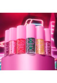 Six flacons de gloss à lèvres avec des capuchons roses, de couleurs variées incluant du rose, du rouge, du vert et du jaune, exposés sur un piédestal rose.