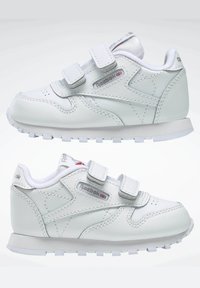 Hvite lær sneakers med borrelåsreimer, teksturerte overflater og en polstret såle. Har sølvmerke-logo og perforerte tær for pusteevne.