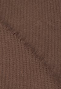 Tissu brun texturé avec un motif en chevrons, présentant des bords effilochés. Le matériau semble doux et est tissé de manière serrée.