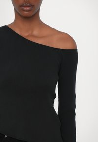 Must mustriba pika varrukaga topp, millel on asümmeetriline õlast avatud kaelus, omades kinnist siluetti ja siledat tekstuuri.