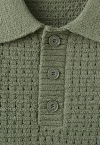 Gros plan sur un vêtement en tricot vert avec un col et trois boutons assortis sur le devant.