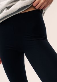 Mustad retuusid, mis on valmistatud venivast materjalist, omavad sileda tekstuuri ja kõrget vööd, mis on osaliselt nähtav halli topi all.