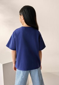 Camiseta de algodón azul con mangas cortas y un corte holgado, combinada con pantalones ligeros a rayas. Diseño sencillo, sin patrones ni acentos visibles.