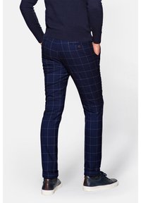 Granatowe spodnie w kratę o dopasowanym kroju, z fakturowanej tkaniny i detalami na tylnej kieszeni, w połączeniu z ciemnymi sneakersami.