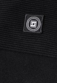 Schwarzer Stoff mit gewebter Textur. Ein quadratischer bestickter Patch zeigt ein kreisförmiges Logo mit einem geometrischen Design in Grau und Weiß.
