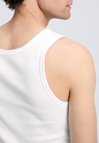 Débardeur côtelé blanc vu de dos, avec de larges emmanchures, un col rond et une texture de tissu lisse.