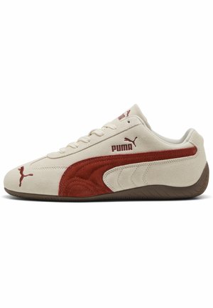Nízky teniska Puma z béžovej semišovej kože s hrdzavo červeným bočným pruhom, hnedou podrážkou a logom Puma na boku, jazyku a špičke.