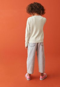 Cremefarvet ribstrik sweater, lyseblå baggy jeans og lyserøde sneakers. Baggrunden er én ensfarvet orange farve.